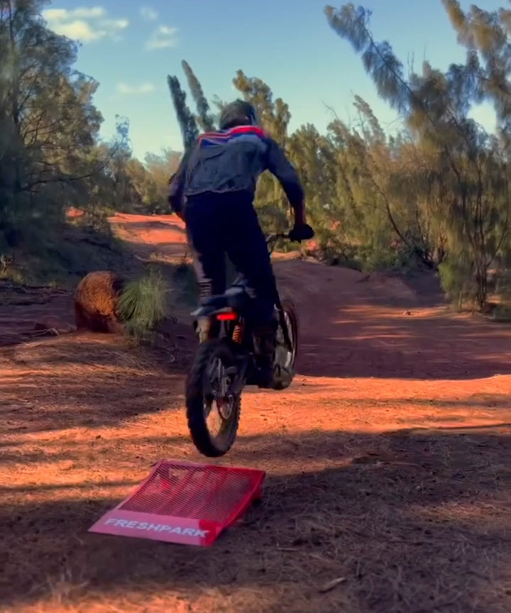 Person riding a bike over a red Freshpark pad in a desert setting