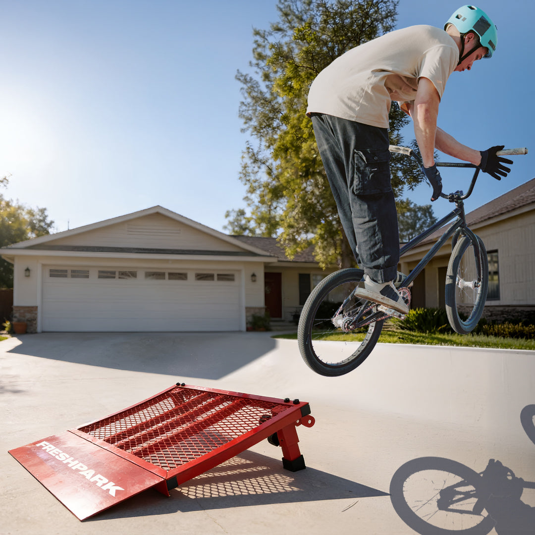 Person on a bicycle performing a trick over a red ramp in a driveway.