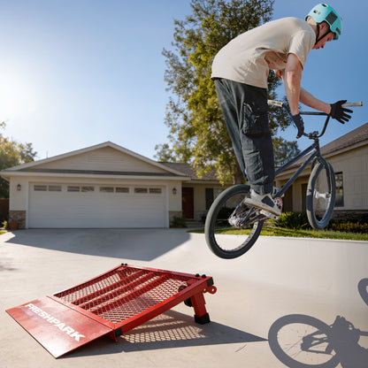 Person on a bicycle performing a trick over a red ramp in a driveway.
